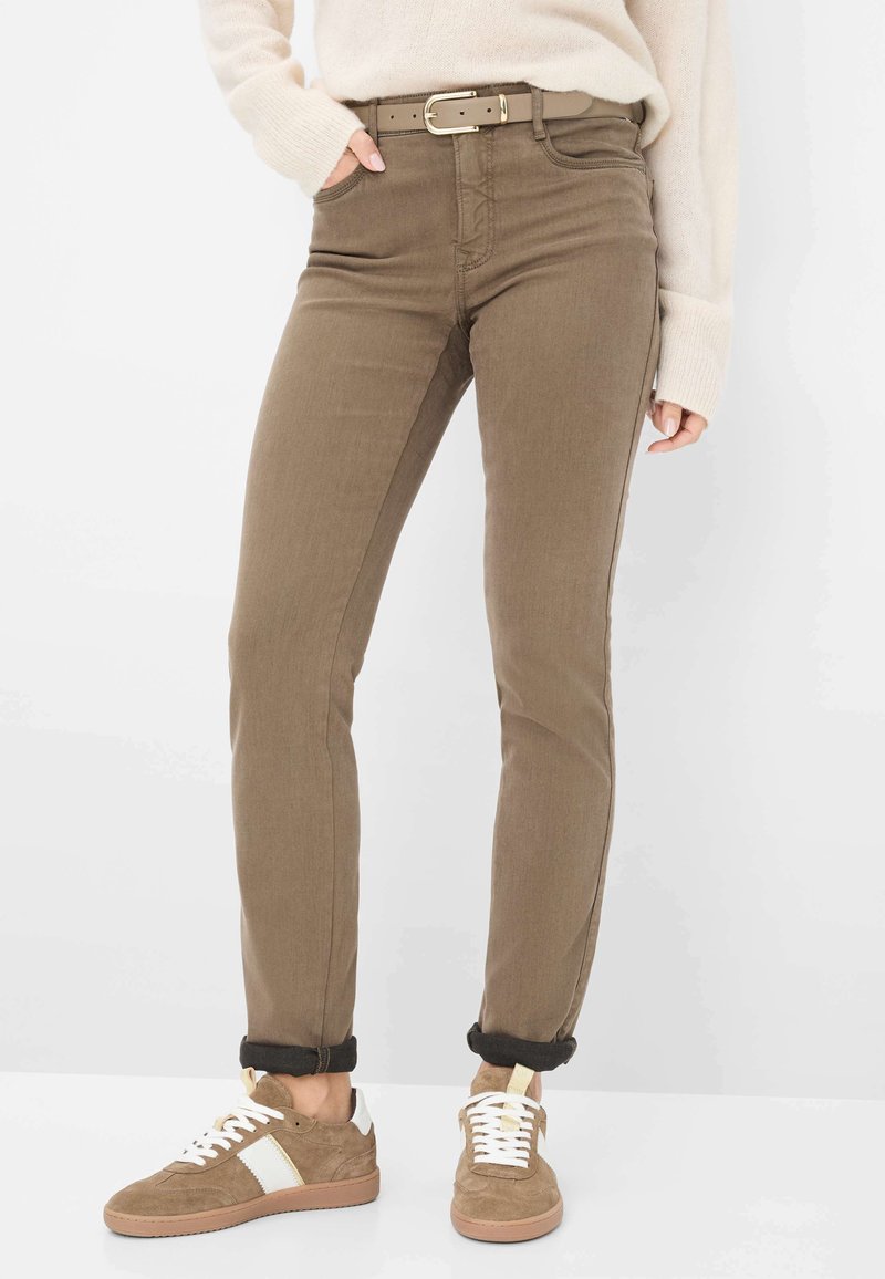Jeans marroni aderenti con una cintura abbinata. Materiale in cotone, stile classico a cinque tasche e orli arrotolati. Sneakers color beige con accenti bianchi.