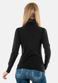 Maglione nero a maniche lunghe con colletto alto a coste, spalle a palloncino e design aderente, abbinato a jeans in denim blu con dettagli sulle tasche posteriori.