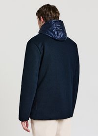 Marineblauer Mantel mit strukturiertem Körper und glänzender gesteppter Kapuze. Hat einen geraden Schnitt, Seitennähte und ein minimalistisches Design.