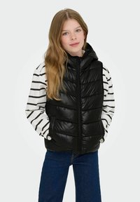 Crni, visok dukserica sa patentnim zatvaračem i kapuljačom, nosi se preko bijele i crne prugaste majice s dugim rukavima. Plave traperice upotpunjuju odjevnu kombinaciju.