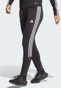 Zwarte sportbroek met een witte drie-strepenontwerp langs de zijkanten. Heeft een aansluitende pasvorm en een trekkoord in de taille voor comfort.