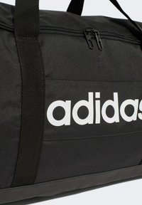 Black duffel bag made of durable fabric, featuring a double zipper, adjustable shoulder strap, and large white "adidas" logo on the side.