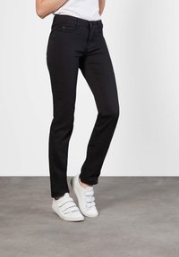 Sorte tettsittende jeans med en glatt tekstur, fem lommer og subtile sømdetaljer, kombinert med hvite borrelås-sneakers.