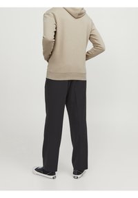 Sudadera beige con capucha y puños acanalados, combinada con pantalones negros de corte holgado y zapatillas negras casuales con suelas blancas.