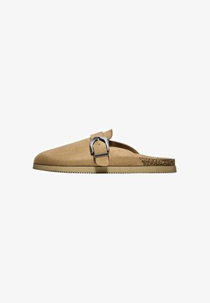 Mule beige en daim à enfiler avec une large sangle à boucle argentée et une semelle intérieure en liège avec une semelle extérieure en caoutchouc rainurée.