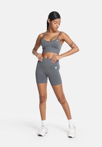 Súprava šedého športového podprsenky a vysokých šortiek, vyrobená z textúrovanej tkaniny. Vyznačuje sa úzkymi ramienkami a logom na prednej strane oboch kusov.