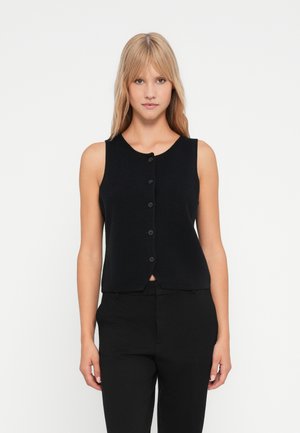 Schwarze gestrickte ärmellose Weste mit rundem Halsausschnitt und sieben Knöpfen vorne, taillierte Passform, kombiniert mit schwarzen Hosen.