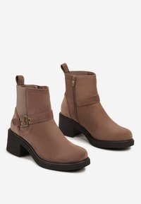 Bottes brunes jusqu'à la cheville en matériau suédé lisse, avec une fermeture éclair sur le côté, un accent de boucle et un large talon noir.