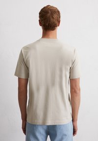 Light beige crew-neck t-shirt with short sleeves, made of smooth cotton material, features a relaxed fit and minimalistic design.