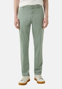Lichtgroene slim fit broek, gemaakt van een gladde stof. Heeft een platte voorkant en een standaard tailleband. Gecombineerd met witte sneakers.