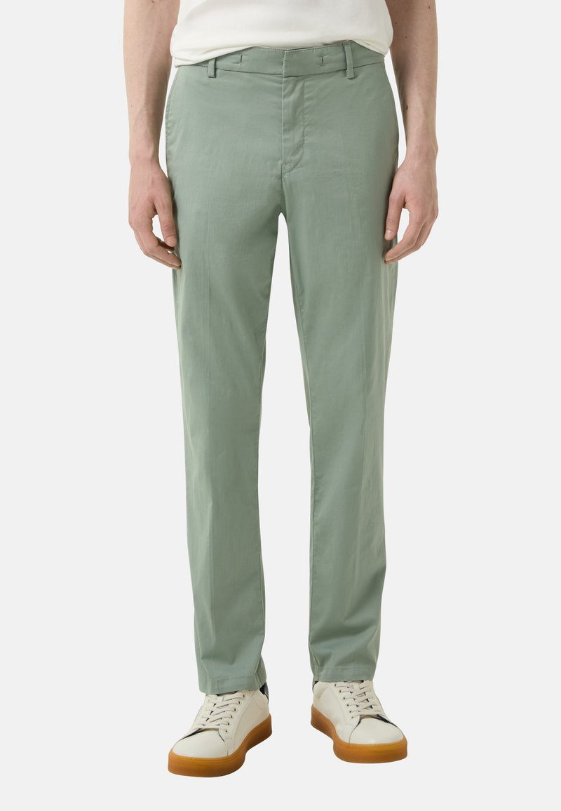 Lichtgroene slim fit broek, gemaakt van een gladde stof. Heeft een platte voorkant en een standaard tailleband. Gecombineerd met witte sneakers.