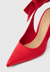 Rød satin stilet med spids tå og udskæringsdesign. Har en bred satin sløjfe bagpå og en tekstureret beige indersål.