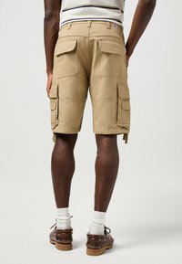 Kha k cargo shorts med flera fickor, rak skärning och förstärkt sömnad. Bärs med vita strumpor och bruna skor.