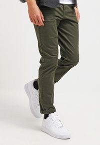 Olivgröna bomullbyxor med slim fit och uppvikt nederkant, kombinerade med vita sneakers i slät lädertextur.