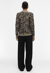 Pull en imprimé léopard dans des tons beige et noir, texture tricotée, col rond, avec des poignets et un ourlet côtelés, associé à un pantalon noir ample.