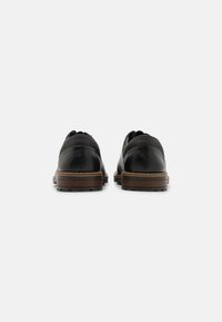 Scarpe in pelle nera con punta tonda, dettagli cuciti e suole in gomma marrone, con una texture liscia e un design minimale.