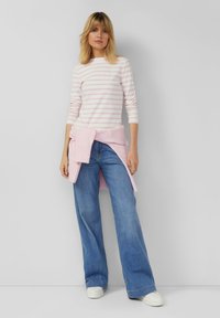 Light pink and white striped long-sleeve top, paired with wide-leg blue jeans, and a soft pink sweater tied at the waist, worn with white sneakers.