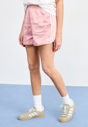 Rosa idrettsshorts med hvite striper, elastisk midje og logo detaljer. Kombinert med grå og hvite joggesko og hvite sokker.