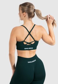 Sujetador deportivo verde oscuro con tirantes cruzados, hecho de un material elástico. Logo "SMILODOX" en blanco en la banda y leggings de talle alto a juego.