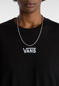 Czarna bawełniana koszulka z zaokrąglonym dekoltem i krótkimi rękawami, z białym haftowanym logo "VANS". Noszona z skręconym srebrnym naszyjnikiem.