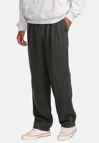 Lässig geschnittene, dunkelgraue, plissierte Hose aus weichem Stoff, mit Seitentaschen und einem bequemen Bund, kombiniert mit weißen Sneakern.