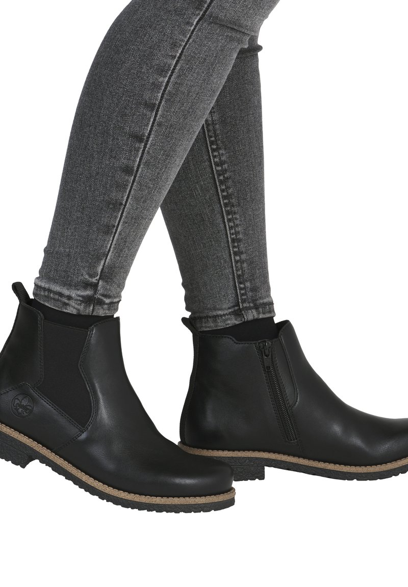 Bottines en cuir noir avec des panneaux élastiques sur les côtés, une fermeture éclair latérale et une semelle en caoutchouc texturé. Présente un détail de couture marron.