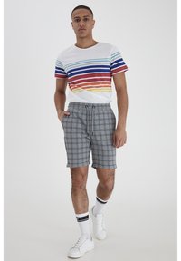 T-shirt blanc à manches courtes avec des rayures horizontales colorées ; short à carreaux gris avec une taille élastique ; baskets blanches avec des accents noirs.