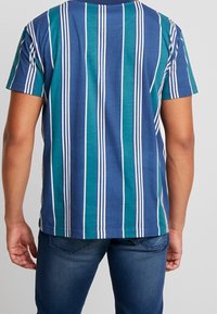 Modro zelené pruhované tričko s krátkým rukávem, s bílými vertikálními pruhy a volným střihem, vyrobené z měkké bavlny.