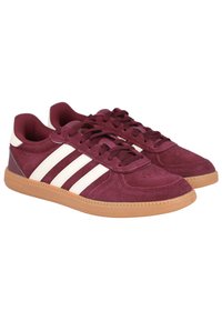 Zapatillas de ante burdeos con diseño de tres rayas blancas, punta redonda y suela de goma. Cuenta con un collar acolchado y un cierre con cordones texturizado.