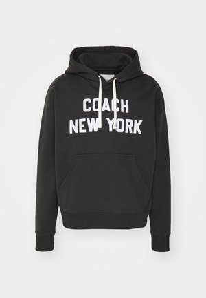 Melns vilnas kapučis, kas izgatavots no mīksta materiāla. Iekļauj priekšējo kabatu, aukliņas un baltu tekstu "COACH NEW YORK" uz krūšu.