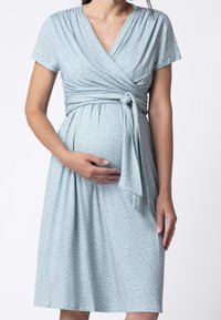 Ljusblå omlotklänning med korta ärmar, vita prickar, knytdekor vid midjan och en flödande kjol ovanför knäet. Mjuk, stretchig tyg.