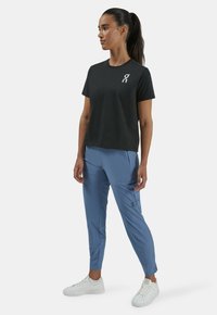 Black short-sleeve T-shirt with a white logo, paired with light blue tapered pants featuring a side zip pocket, worn with white sneakers.