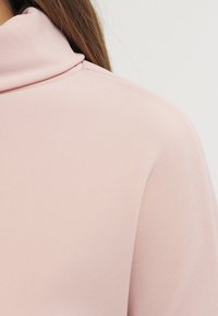 Rosa gerippter Stoff mit hohem Kragen, der eine glatte Textur und eine figurbetonte Passform zeigt und einen zeitgemäßen Stil betont.