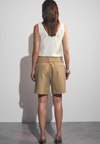 Lichtbeige shorts met een op maat gemaakte pasvorm, gecombineerd met een witte gebreide top met een geometrisch open patroon en een ruime rug.