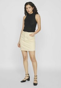Top de punto negro sin mangas y minifalda de mezclilla beige, con bolsillos laterales. La modelo lleva unos zapatos negros de tacón bloque con tiras.