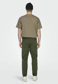 Zielone oliwkowe bawełniane spodnie w połączeniu z luźnym beżowym t-shirtem; uzupełnione czarną dzianinową czapką beanie i białymi trampkami.