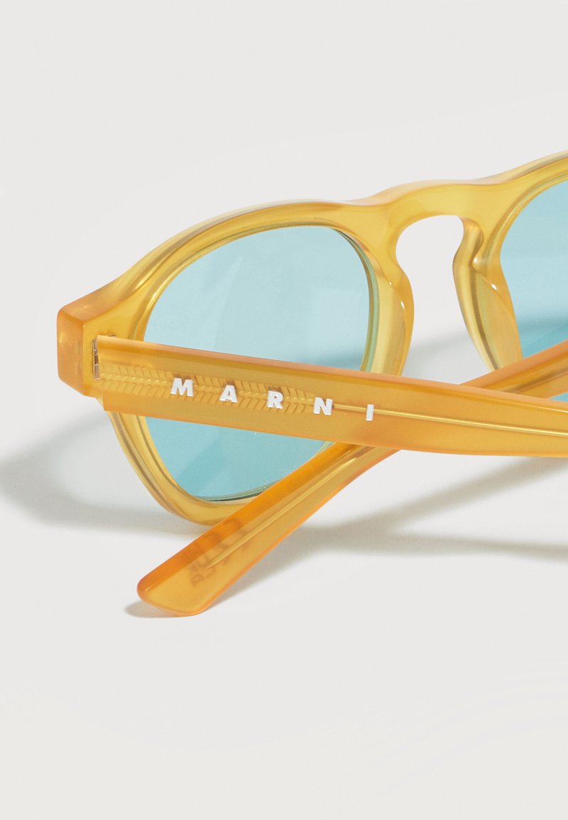 Occhiali da sole traslucidi gialli con lenti blu, con il marchio "MARNI" inciso sull'asta.