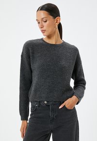 Maglione a costine grigio antracite con collo rotondo e maniche lunghe, realizzato in materiale morbido. Abbinato a jeans neri, con una vestibilità rilassata.