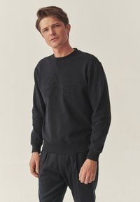 Czarna bluza z wytłaczanym tekstem, z okrągłym dekoltem, �ściągaczami przy mankietach i na dole. Miękka tkanina o prostym kroju i minimalistycznych detalach.