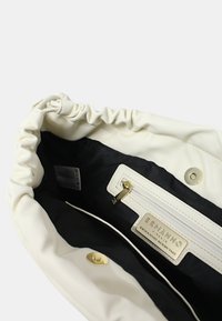 Borsa a sacchetto in tessuto bianco con interno nero. Presenta una tasca con zip, dettagli in oro e un'etichetta del marchio all'interno con testo in rilievo.