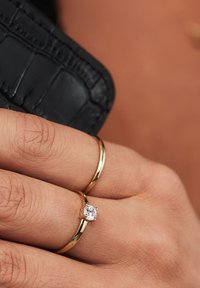 Goldringe an einer Hand, einer davon mit einem einzelnen klaren Edelstein. Die Ringe sind schlicht mit einer glatten Textur vor einem dunklen Hintergrund.