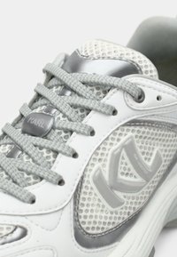 Fehér tornacipő szürke hálós panelekből, fűzőkkel és részletekkel. Texturált, fényes logóval és támogató talppal rendelkezik.