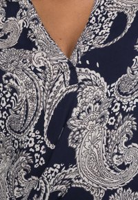Primo piano di un tessuto blu navy con dettagliati motivi paisley e floreali bianchi su un collo di un indumento.