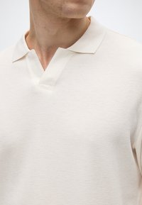 Ανοιχτό μπεζ πόλο μπλουζάκι με υφή που μοιάζει με βαμβακερό δίχτυ. Διαθέτει κλασικό γιακά με V-λαιμόκοψη. Μαλακό ύφασμα με άνετη εφαρμογή.