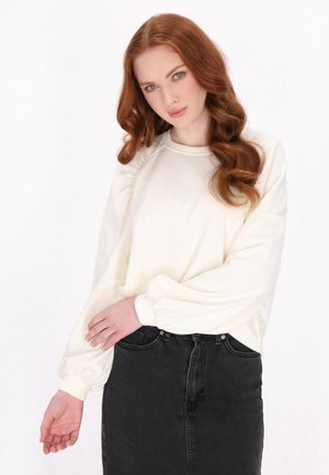 Felpa color crema con maniche a sbuffo e scollo tondo, abbinata a una gonna di jeans nera. Texture liscia, design casual.