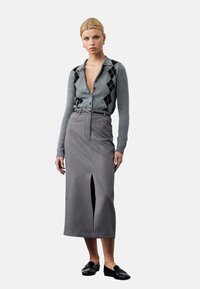 Grå cardigan med sort argyle-mønster, knappet, parret med en grå, knælang nederdel med en frontslids. Sorte loafers fuldender looket.