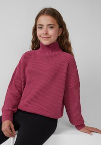 Sweter z golfem, dzianiny w głębokim różu z fakturowanym wzorem i opuszczonymi barkami, zestawiony z czarnymi legginsami. Prosty, casualowy krój.
