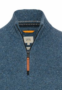 Blauer Strickpullover mit hohem Kragen, halbem Reißverschluss, kontrastierendem orangefarbenem Innenfutter und Lederzipp-Anhänger. Etikett innen sichtbar.