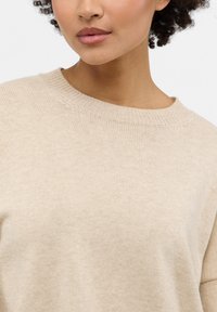 Maglione beige a maglia con scollatura a girocollo a costine, texture morbida e vestibilità rilassata, che mette in risalto linee pulite e design minimali.