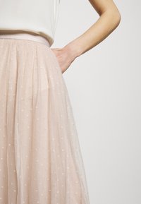 Jupe en tulle rose pâle avec une ceinture ajustée et de délicats motifs d'étoiles brodées sur tout le tissu, créant un aspect doux et texturé.